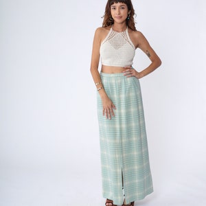 May include: A woman wearing a white crochet halter top and a long, light blue and white plaid skirt with a slit up the front. She is wearing brown heeled sandals.