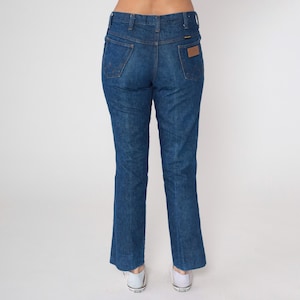 May include: Blue denim jeans with a classic fit, featuring a high waist and a straight leg. The jeans have traditional five-pocket styling, belt loops, and a brown leather patch on the back. The denim has a medium wash with subtle fading.