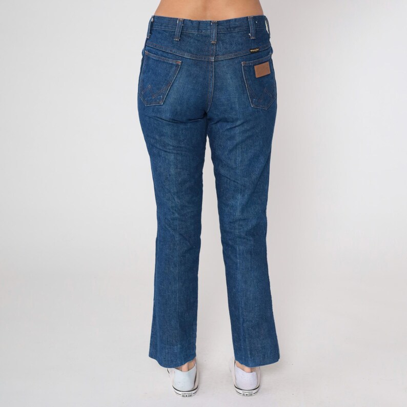 May include: Blue denim jeans with a classic fit, featuring a high waist and a straight leg. The jeans have traditional five-pocket styling, belt loops, and a brown leather patch on the back. The denim has a medium wash with subtle fading.