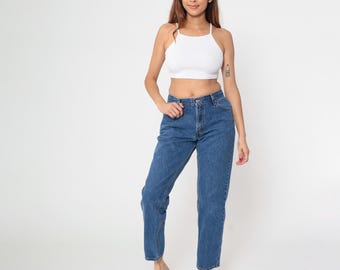 May include: A woman wearing a white halter top and blue denim jeans. The jeans have a classic, straight-leg fit. The woman is also wearing white sneakers. The background is plain white.