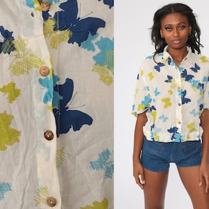 May include: A white button-down shirt with a short sleeve and a butterfly print in shades of blue, green, and white.