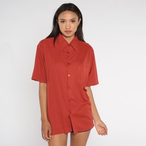 May include: A rust-colored short-sleeved button-down shirt with a wide collar.