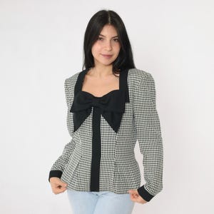 May include: A black and white gingham blazer with a large black bow at the neckline. The blazer has long sleeves and a fitted silhouette.