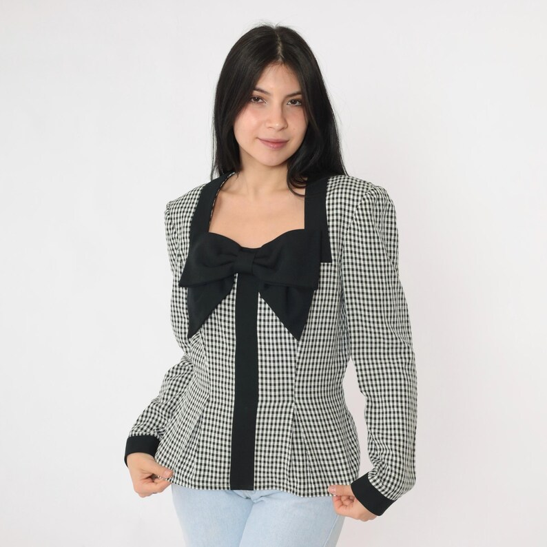 May include: A black and white gingham blazer with a large black bow at the neckline. The blazer has long sleeves and a fitted silhouette.