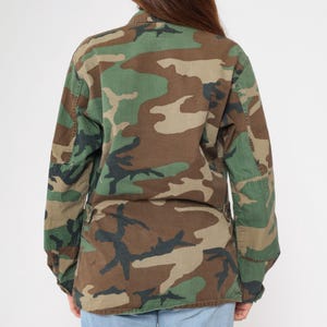 May include: A green, brown, and black camouflage jacket with long sleeves and a button-up front.