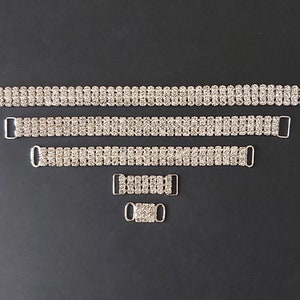 May include: Four silver rhinestone bra straps of varying lengths. The straps are made of metal with a row of clear rhinestones.