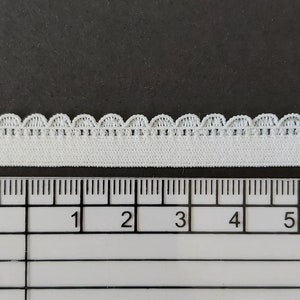 Pu&ograve; includere: Finitura elastica bianca con bordo a festoni. La finitura &egrave; misurata su un righello che mostra 17,8 cm.