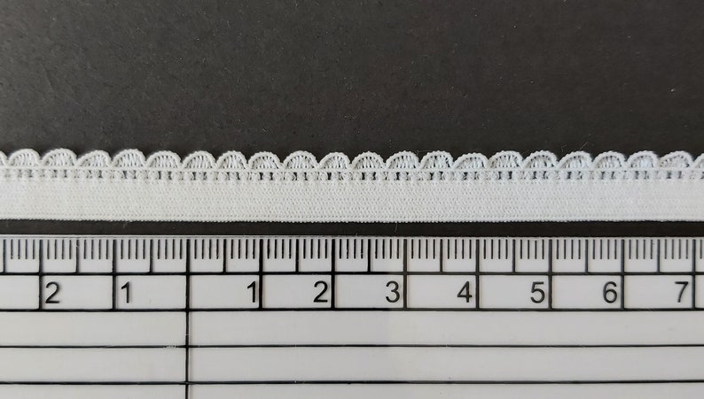 Pu&ograve; includere: Finitura elastica bianca con bordo a festoni. La finitura &egrave; misurata su un righello che mostra 17,8 cm.