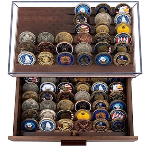 May include: A wooden display case with a clear acrylic cover, filled with numerous collectible coins. The coins are arranged in rows, showcasing various designs and colors, including gold, silver, and bronze tones. The case has a drawer for additional storage.