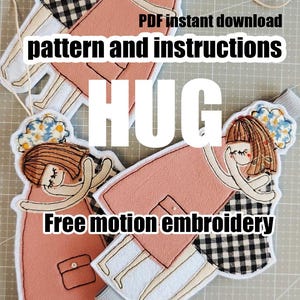 Può includere: Bambole di stoffa ricamate in posa abbracciata, con cappotto rosa e gonna a quadri bianchi e neri. Le bambole hanno i capelli castani e sono decorate con elementi floreali. Il testo sull'immagine recita "HUG" e "Free motion embroidery".