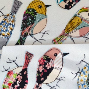 May include: A collection of fabric bird appliqu&eacute;s in various colors and patterns. The birds feature floral, polka dot, and striped designs, with black stitched outlines and delicate wire legs. The background is a soft white.