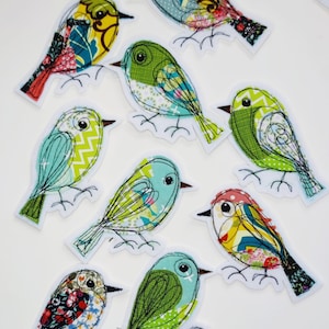 May include: A collection of nine colorful bird patches with intricate fabric patterns and embroidered details. Each bird features a unique design with various colors, including green, blue, yellow, and red, and is outlined with black stitching.