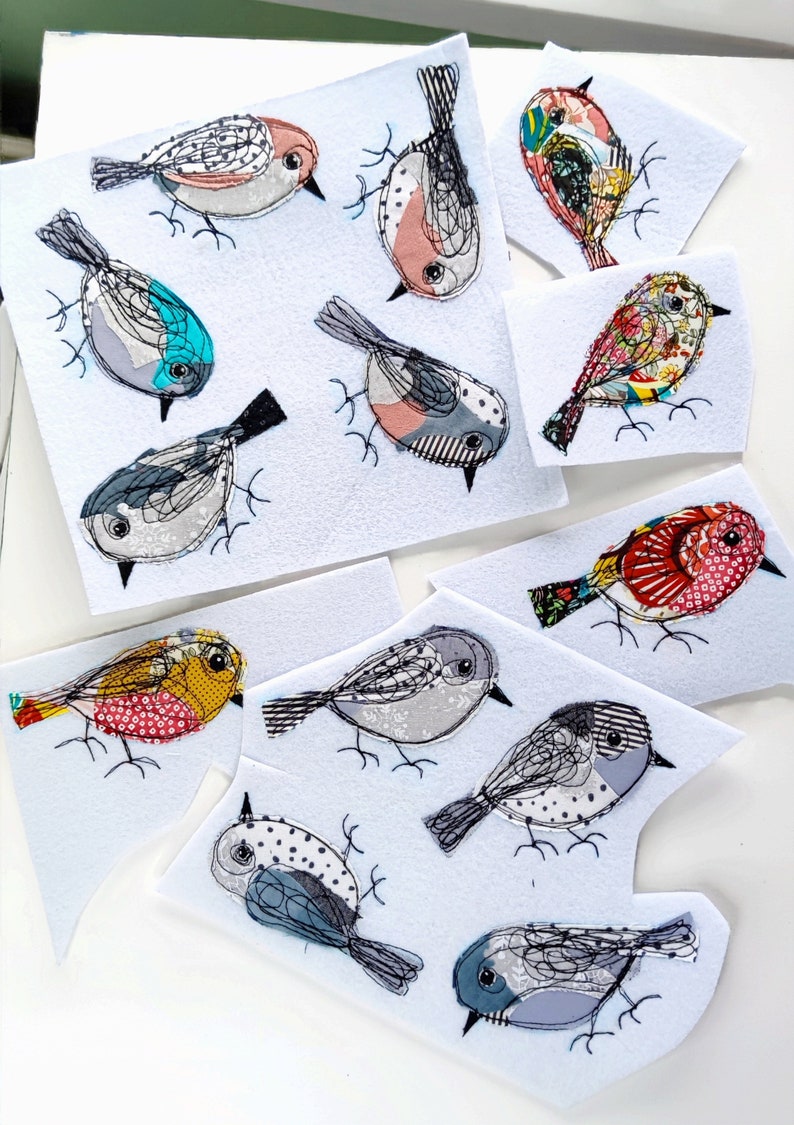 May include: A collection of fabric bird appliqu&eacute;s in various colors and patterns. Each bird features detailed stitching, with designs including stripes, polka dots, and floral prints. The birds are on white felt cutouts, creating a whimsical, handcrafted aesthetic.