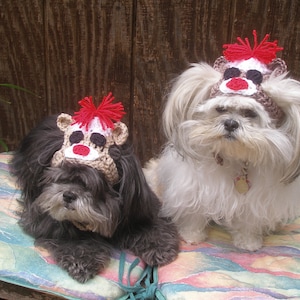 May include: Two small dogs wearing crocheted reindeer hats. The dog on the left is black and the dog on the right is white. Both dogs are looking at the camera.