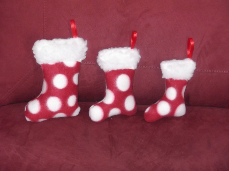 May include: Three red and white polka dot Christmas stockings with white faux fur trim. The stockings are hanging on a red couch.