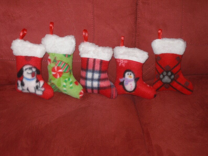 May include: Five red Christmas stockings with white fur trim. Each stocking features a different design: a dog, candy canes, plaid, a penguin, and a paw print.