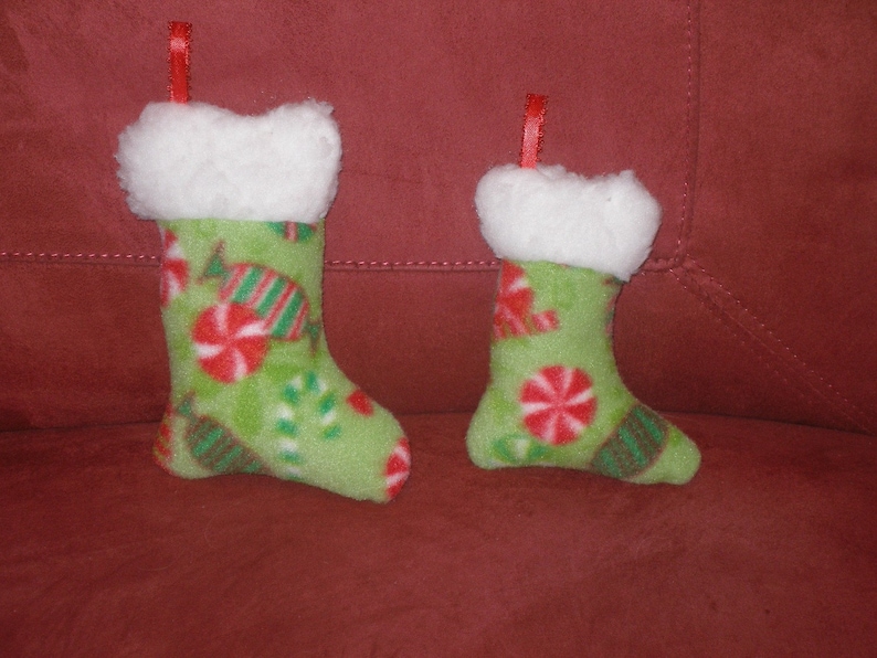 May include: Two green and white Christmas stockings with a candy cane and peppermint design. The stockings have a white fluffy cuff and red ribbon.