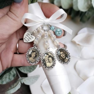 Può includere: Un ciondolo per bouquet da sposa con tre cornici ovali color argento contenenti foto in bianco e nero, perle bianche, una perla azzurra e un ciondolo a forma di cuore in argento con l'incisione you are always in my heart.