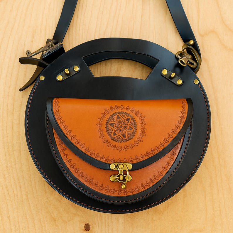 Handmade round crossbody bag crafted from black and brown genuine leather, featuring a Turkish floral motif burned and painted by hand. Elegant, structured, and artisan-made—this boho shoulder purse combines traditional design with practical use. A unique accessory from Türkiye.