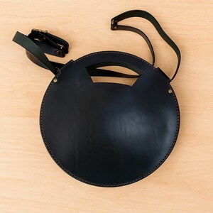 Handmade round crossbody bag crafted from black and brown genuine leather, featuring a Turkish floral motif burned and painted by hand. Elegant, structured, and artisan-made—this boho shoulder purse combines traditional design with practical use. A unique accessory from Türkiye.