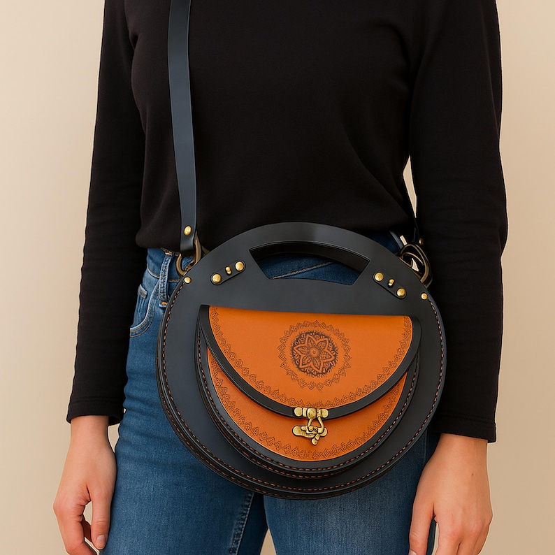 Handmade round crossbody bag crafted from black and brown genuine leather, featuring a Turkish floral motif burned and painted by hand. Elegant, structured, and artisan-made—this boho shoulder purse combines traditional design with practical use. A unique accessory from Türkiye.