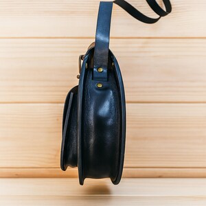 Handmade round crossbody bag crafted from black and brown genuine leather, featuring a Turkish floral motif burned and painted by hand. Elegant, structured, and artisan-made—this boho shoulder purse combines traditional design with practical use. A unique accessory from Türkiye.