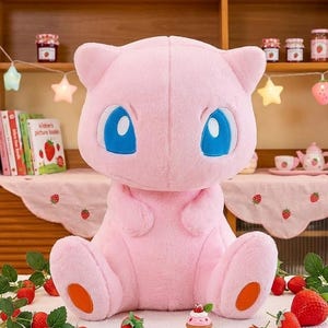 May include: A large, pink plush toy of a cartoon character with large blue eyes and orange accents on its feet. The plush is sitting in front of a shelf with books, jars, and decorative lights. Strawberries and strawberry decorations are in the foreground.