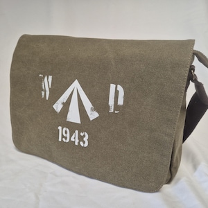 Könnte beinhalten: Olivgrüne Messenger Bag mit Klappenverschluss. Die Tasche hat ein weißes Grafikdesign mit dem Text "W A D" und der Zahl "1943" auf der Vorderseite. Die Tasche hat einen Schultergurt und einen Schnallenverschluss.