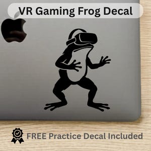 May include: Black vinyl decal of a frog wearing a VR headset, with the text "VR Gaming Frog Decal" above. The decal is on a gray surface. The text "FREE Practice Decal Included" is below.