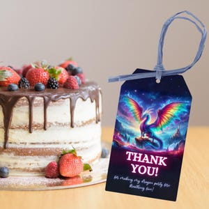Peut inclure: Une &eacute;tiquette avec un dragon color&eacute; et l'inscription "THANK YOU!" est attach&eacute;e avec un ruban bleu. Un g&acirc;teau avec gla&ccedil;age au chocolat et fruits frais est en arri&egrave;re-plan.