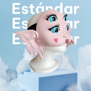 May include: Pink mask with three eyes, two of which are blue and one is green, and a pink heart on the cheek. The mask has large pink wings and is on a white mannequin head.