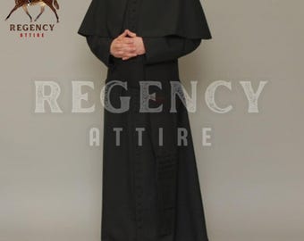 May include: A black cassock with a long, flowing skirt and a cape collar. The cassock has a row of buttons down the front and a small pocket on the left side. The cassock is worn by a person standing in front of a plain white background.