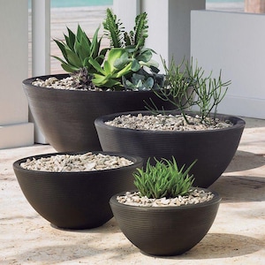 May include: Four dark brown, ribbed, round planters of varying sizes, each filled with small stones and different types of green succulents and plants. The planters are arranged on a light-colored surface.