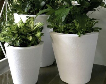 May include: Three white, textured, cone-shaped planters filled with lush green plants. The planters vary in size, with the largest in the background and the smallest in the foreground. The plants have large, vibrant green leaves, creating a contrast with the white planters.