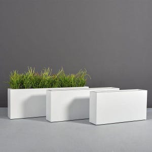 May include: Three rectangular white planters, two empty and one filled with green grass. The planters are arranged in a row, with the grass-filled planter on the left. The background is a solid gray.