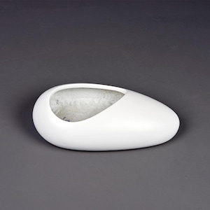 May include: A white, oval-shaped decorative bowl with a smooth, glossy finish. The bowl has a large, asymmetrical opening on the top, revealing a textured interior. The design is minimalist and modern, suitable for home decor.