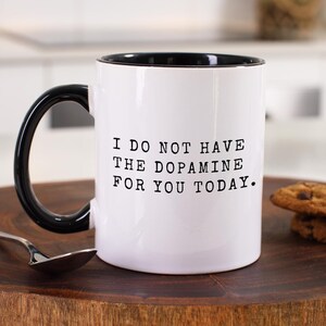 May include: White ceramic coffee mug with a black rim and handle. The mug has black text that reads "I do not have the dopamine for you today."