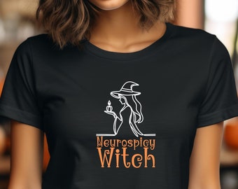 May include: A black t-shirt with a white graphic of a witch holding a candle. The text "Neuroscipy Witch" is printed in orange below the graphic.