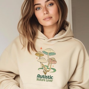 May include: A beige hoodie with a graphic of mushrooms and the text "Autistic Nature Lover" printed on the front.