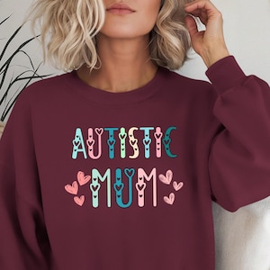 May include: Burgundy sweatshirt with the text "AUTISTIC MUM" in colorful letters with hearts around the words.