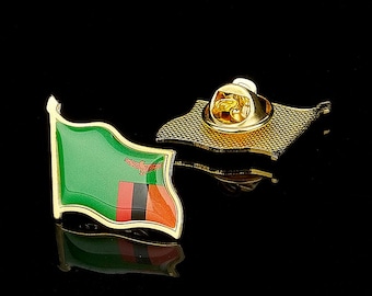 Puede incluir: Un pin de solapa de metal dorado con forma de bandera de Zambia ondeando. El pin presenta un campo verde con un águila roja y un patrón de franjas verticales en rojo, negro y naranja en la esquina inferior. La parte trasera incluye un cierre.