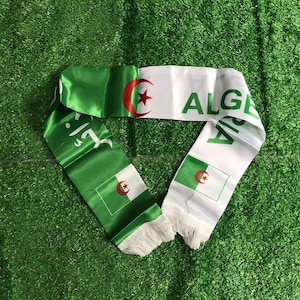 Peut inclure: Une écharpe en satin aux couleurs verte et blanche du drapeau algérien. L'écharpe présente l'emblème du croissant et de l'étoile rouges, le texte ALGERIA en lettres capitales vertes et des franges blanches aux deux extrémités de l'accessoire.