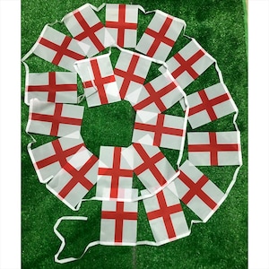 May include: A string of rectangular bunting flags featuring the flag of England, which consists of a red cross centered on a white background. The flags are connected by a thin white cord, arranged in a circular pattern with multiple individual pennants.