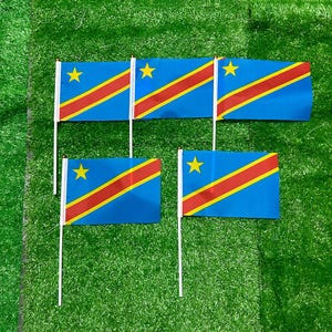 May include: Five small handheld flags of the Democratic Republic of the Congo, each featuring a blue field with a yellow star in the upper left corner and a diagonal red stripe bordered by thin yellow lines running from the bottom left to top right.