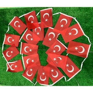 May include: A string of rectangular flags featuring the national flag of Turkey, which consists of a red background with a white crescent moon and a five-pointed star. The flags are connected by a white ribbon and arranged in a circular pattern.