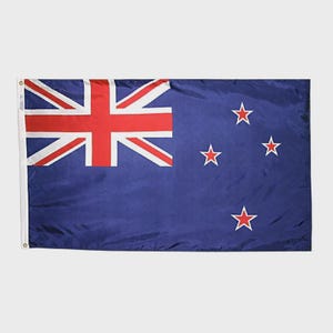 Puede incluir: Una bandera rectangular con fondo azul oscuro, con la Union Jack en la esquina superior izquierda. Cuatro estrellas rojas con contorno blanco están dispuestas a la derecha. La bandera está hecha de un material ligero.