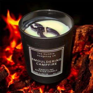 May include: A white ceramic mug with a black handle and the text "But First, Coffee" in a bold, black font. The mug is filled with a dark liquid, probably coffee, and rests on a light-coloured surface.