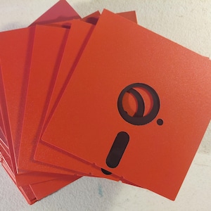 May include: A collection of vibrant orange floppy disks. Each disk features a black design, including a semi-circle and a rectangle. The disks are arranged in a fan shape, displaying their edges and the design on the top disk.