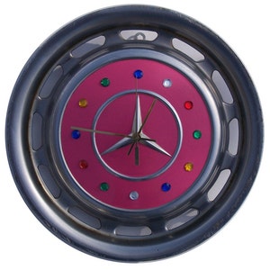 May include: A unique wall clock with a pink face and a silver-colored rim. The clock features colorful gem-like markers and silver hands. The clock's design incorporates a vintage car wheel cover, adding a retro aesthetic.