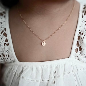 May include: A delicate gold chain necklace with a small, round pendant featuring the letter "H" in a simple, minimalist style.